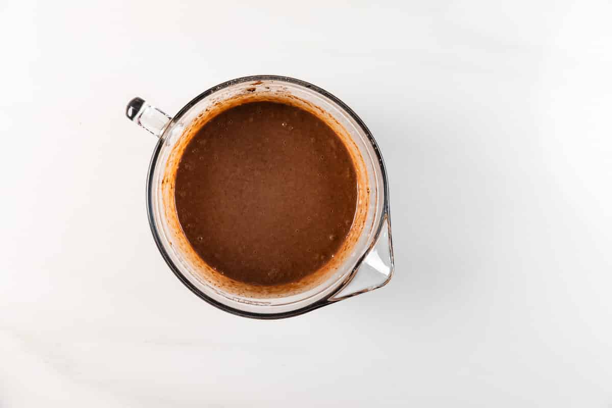 A glass measuring cup filled with a thick, blended brown liquid sits on a white surface, viewed from above.