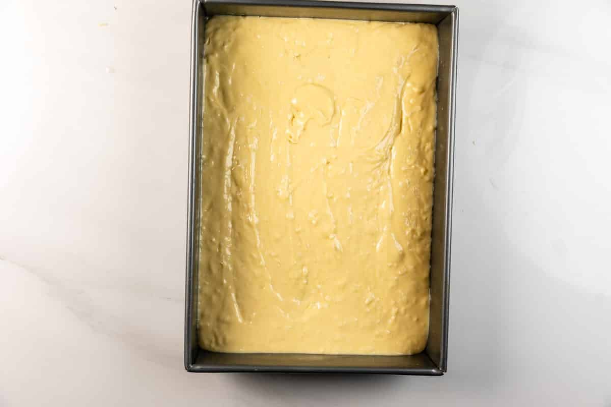 A rectangular metal baking pan filled with smooth, pale yellow cake batter, ready to be baked. The pan is placed on a white countertop.