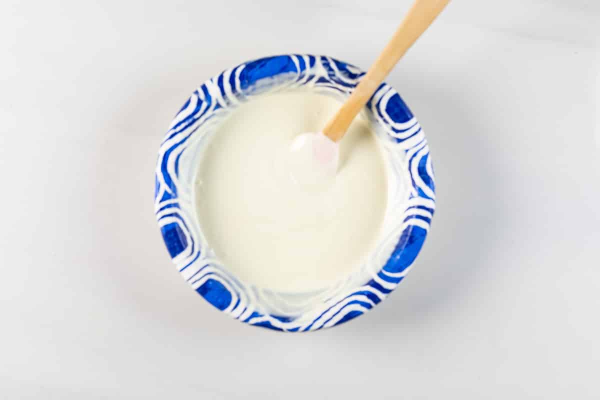 A blue and white patterned bowl filled with white yogurt or cream, with a wooden spoon resting inside, on a white surface.
