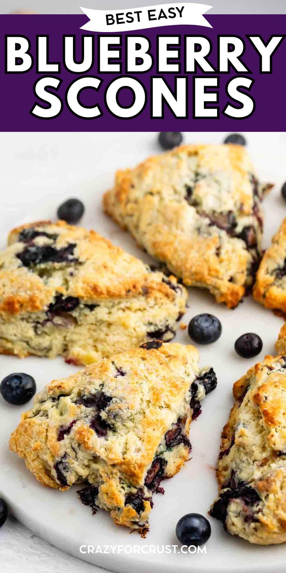Freshly baked golden-brown blueberry scones are arranged on a white plate with a few whole blueberries scattered around. Text above reads Best Easy Blueberry Scones.