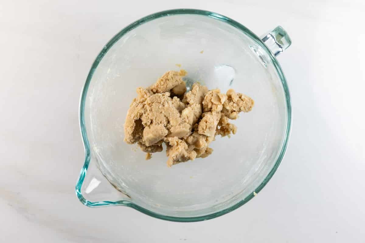 A clear glass mixing bowl containing a partially mixed, beige cookie dough sits on a white countertop.