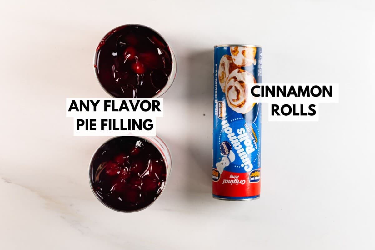 Two open cans of pie filling and a tube of cinnamon rolls are placed on a white surface. The cans are labeled Any Flavor Pie Filling and the tube is labeled Cinnamon Rolls.
