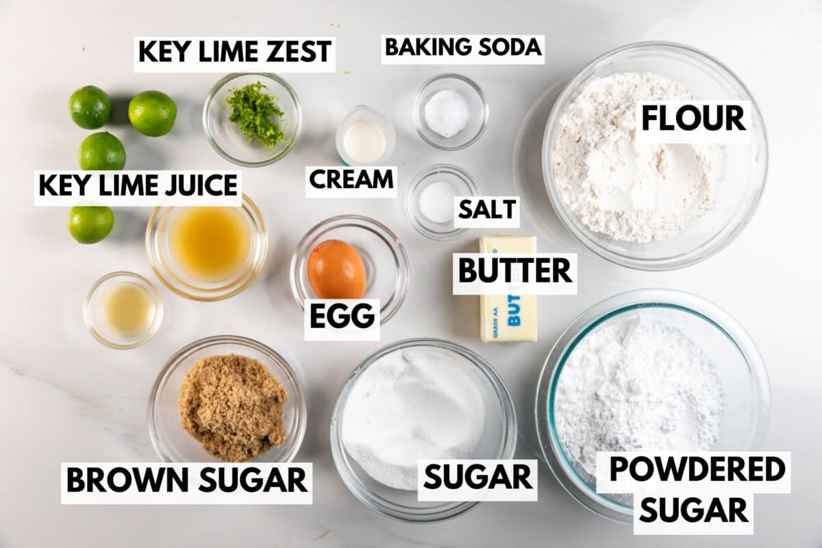 Top-down view of ingredients for baking, including key limes, key lime zest and juice, egg, cream, butter, brown sugar, sugar, powdered sugar, flour, baking soda, and salt, each labeled with text on the image.