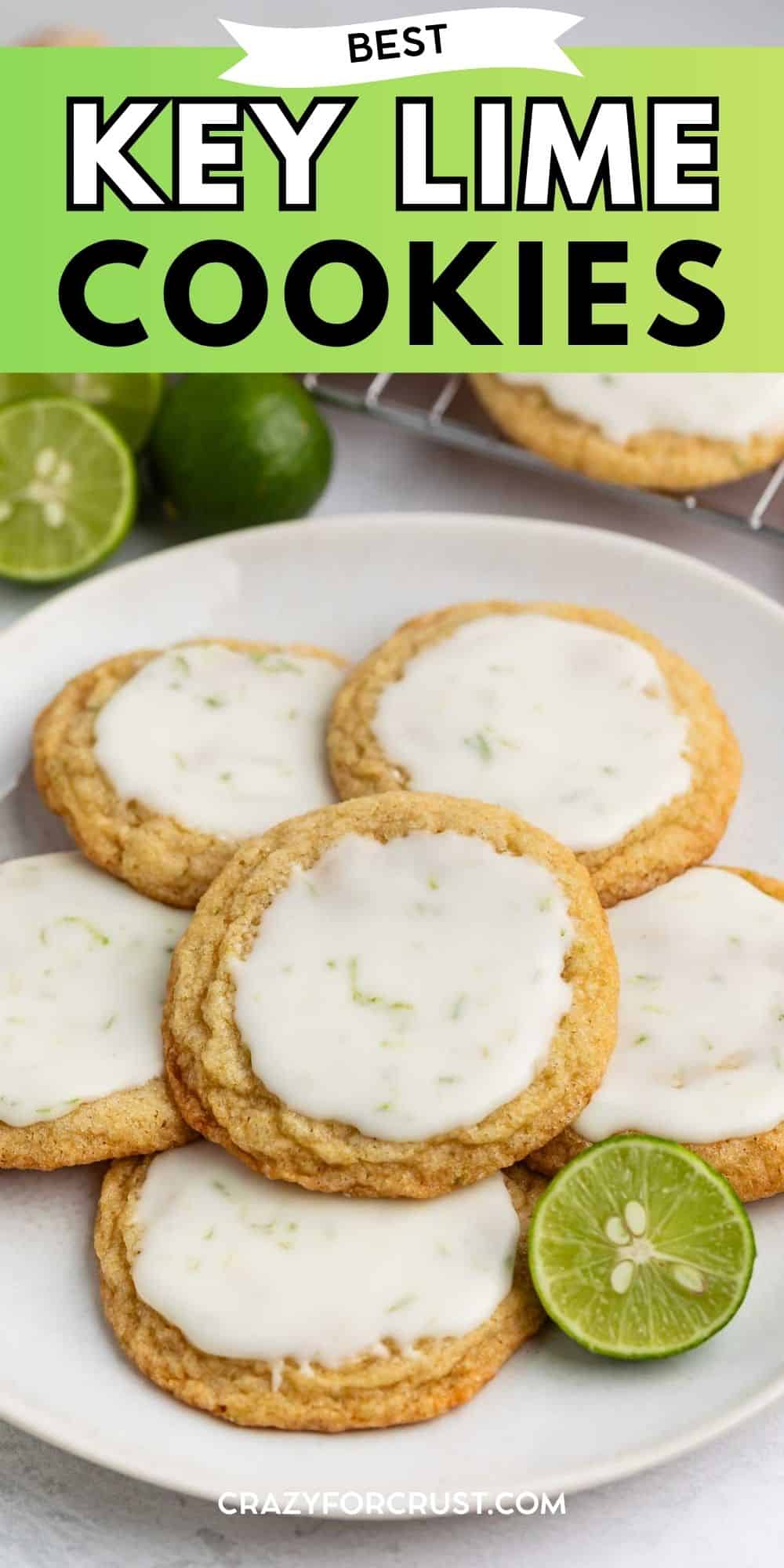 A plate of key lime cookies with white glaze and lime zest, surrounded by fresh limes, on a table. Text at the top reads “Best Key Lime Cookies.”.