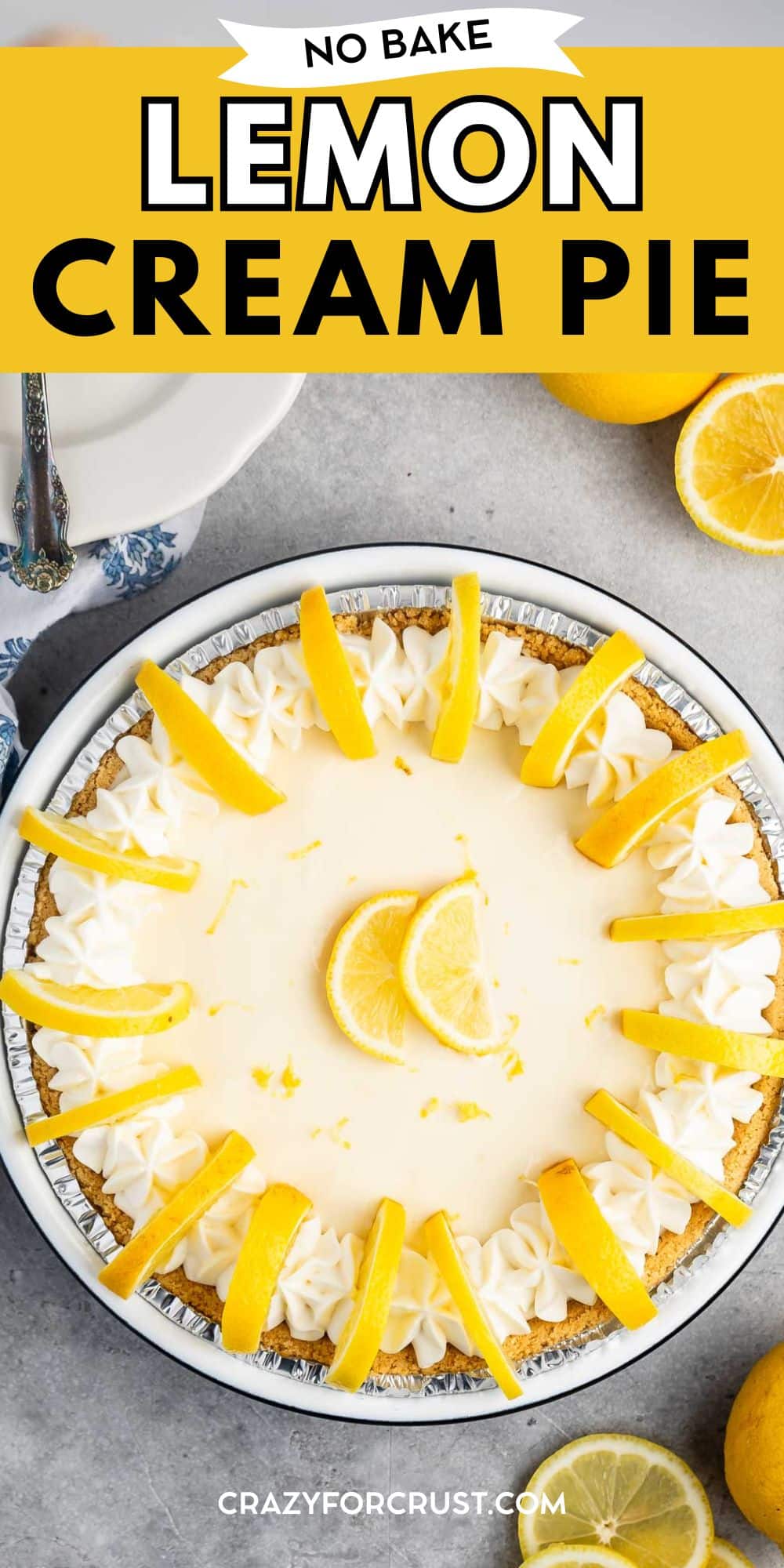 Top-down view of a no-bake lemon cream pie garnished with whipped cream and lemon slices, set on a gray surface with a slice cut out and fresh lemons nearby. Text reads: No Bake Lemon Cream Pie.