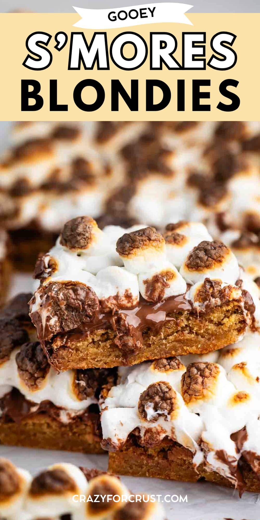 A close-up of gooey s’mores blondies topped with toasted marshmallows and melted chocolate, stacked on a plate. The text above reads, Gooey S’mores Blondies.