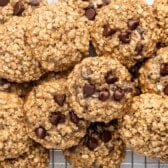 A batch of oatmeal chocolate chip cookies piled on a wire cooling rack, with visible oats and chocolate chips throughout the golden-brown cookies.