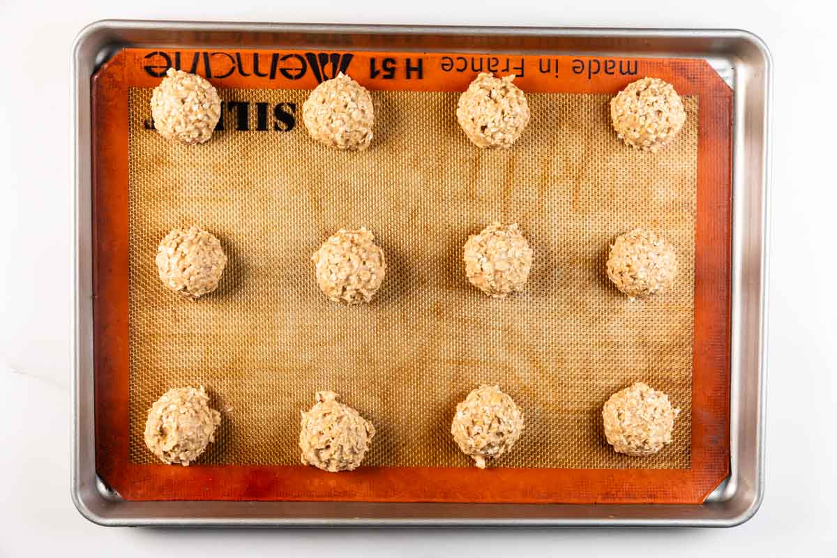 Une plaque à pâtisserie recouverte d'un tapis en silicone contient douze boules de pâte à biscuits non cuites uniformément espacées, disposées dans une grille 3 × 4.