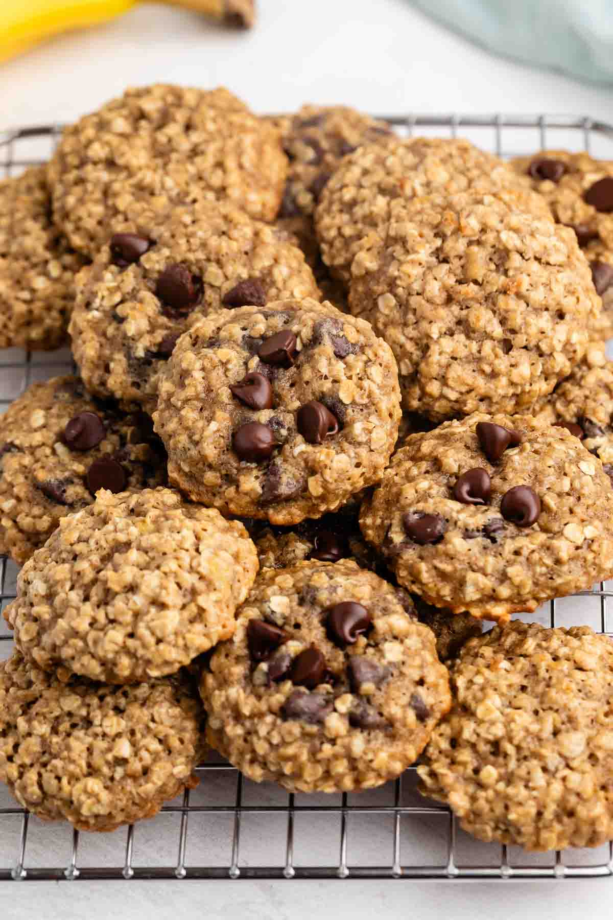 Une pile de biscuits à l'avoine avec des pépites de chocolat repose sur une grille de refroidissement, avec quelques pépites de chocolat visibles sur plusieurs biscuits.