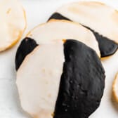 A close-up of black and white cookies, each round cookie glazed half with white icing and half with chocolate icing, arranged on a white surface.