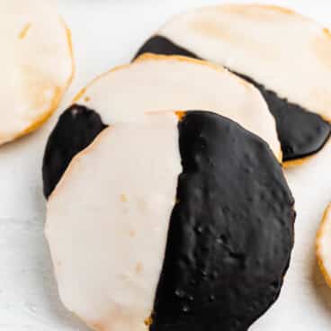 A close-up of black and white cookies, each round cookie glazed half with white icing and half with chocolate icing, arranged on a white surface.