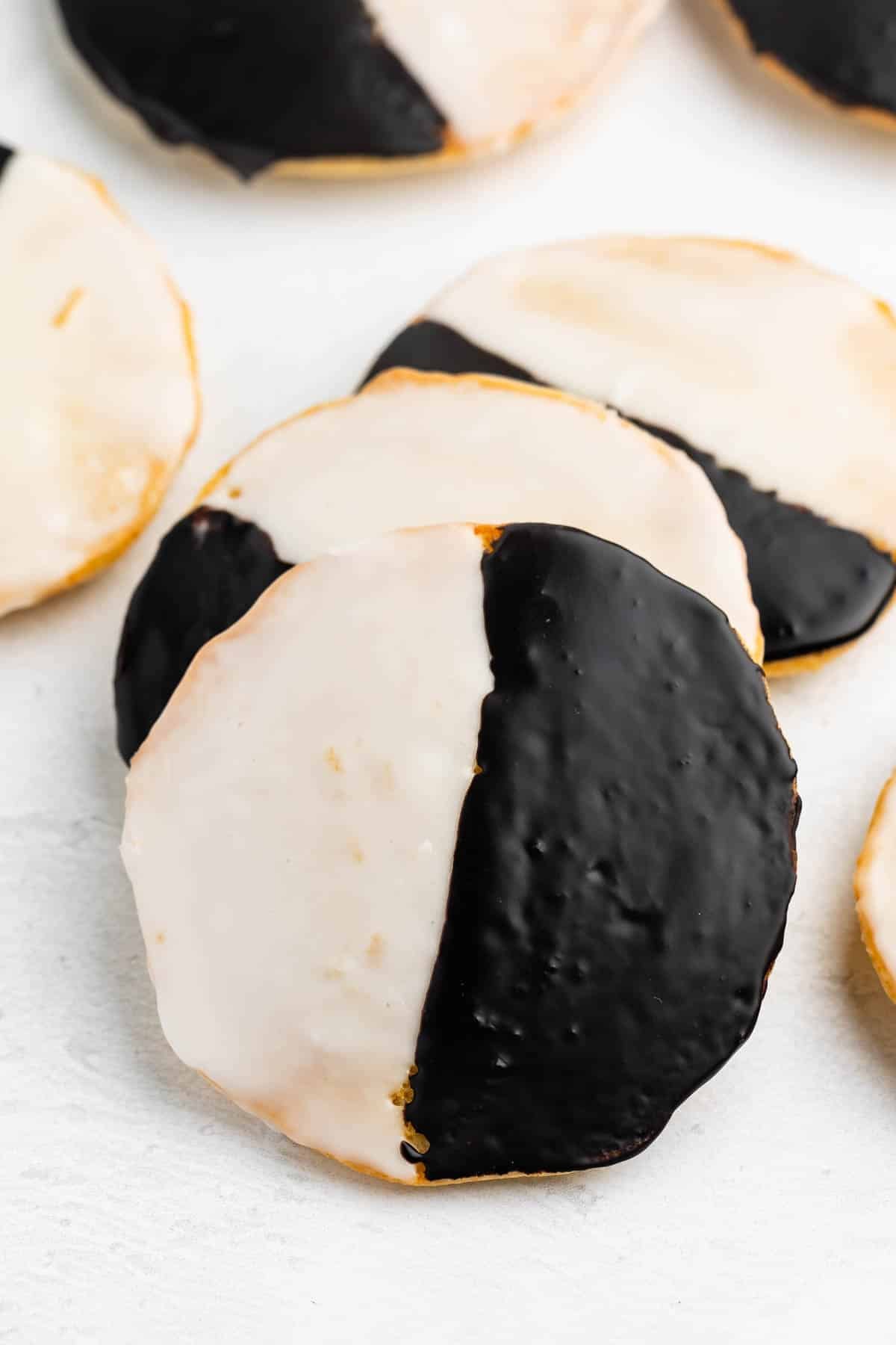 A close-up of black and white cookies, each round cookie glazed half with white icing and half with chocolate icing, arranged on a white surface.