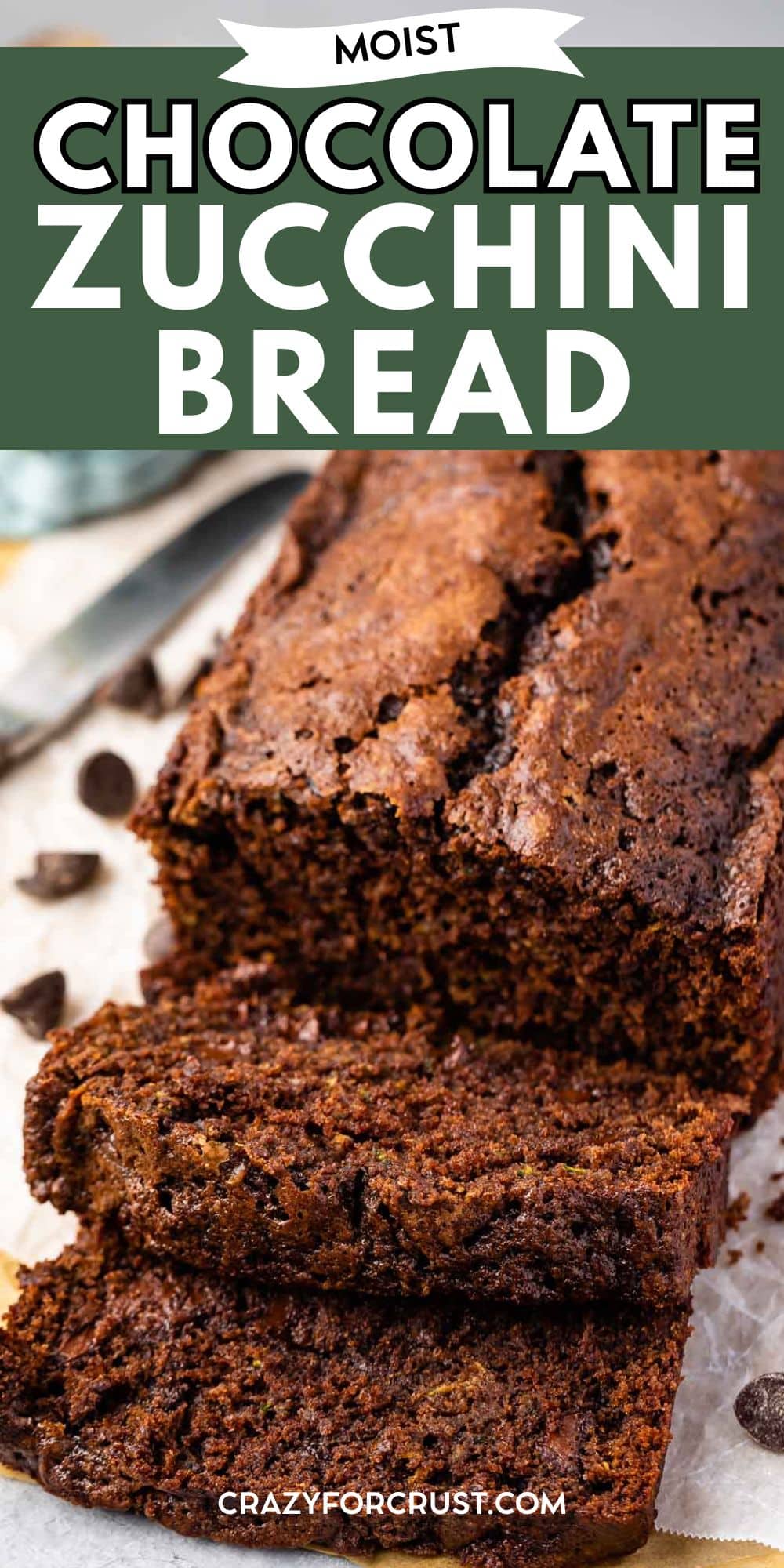 A freshly baked loaf of moist chocolate zucchini bread sits on parchment paper, with two thick slices cut and chocolate chips scattered nearby. The bread has a rich, dark brown color and a soft, textured interior.