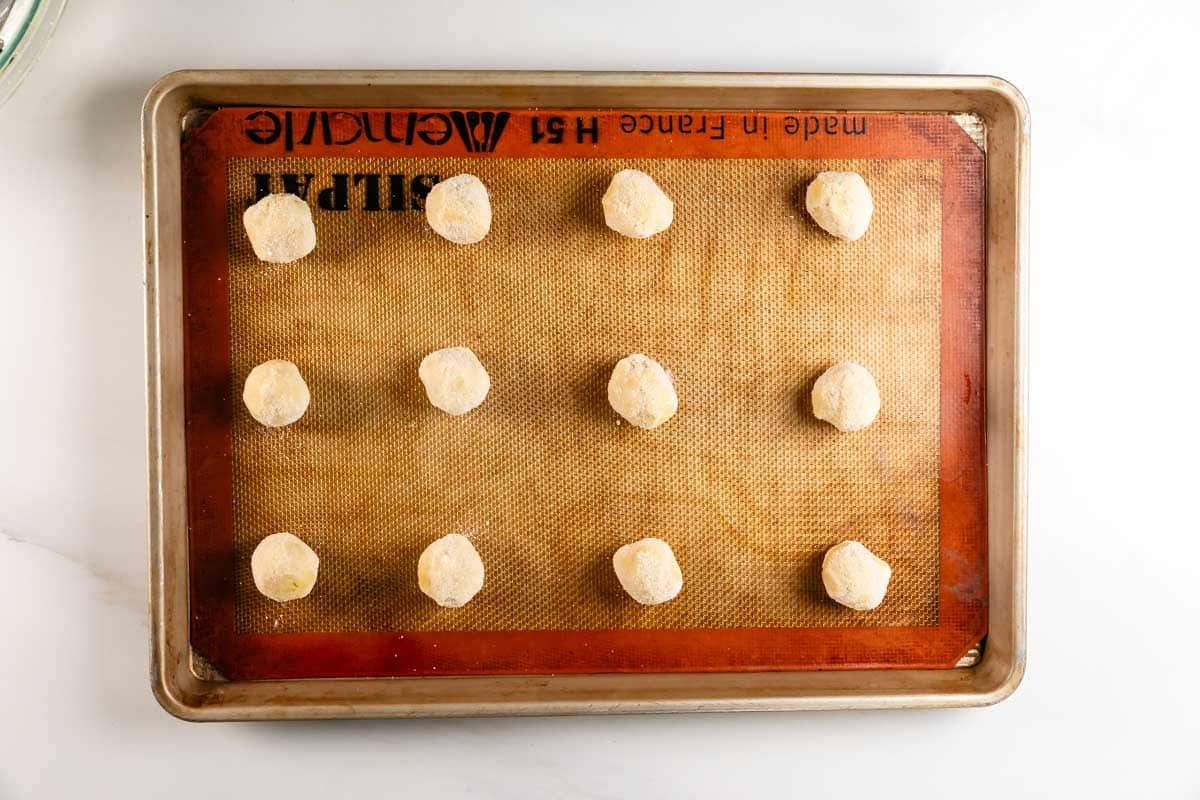 A baking sheet lined with a silicone mat holds twelve evenly spaced balls of cookie dough, ready to be baked.