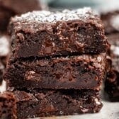 A close-up of three rich, fudgy chocolate brownies stacked on top of each other, with melted chocolate inside and a light dusting of powdered sugar on top.