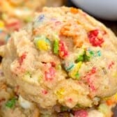 A close-up of a soft, chewy cookie filled with colorful bits of cereal, giving it a vibrant and textured appearance. The cookie looks homemade and has a golden brown color with visible colorful specks throughout.