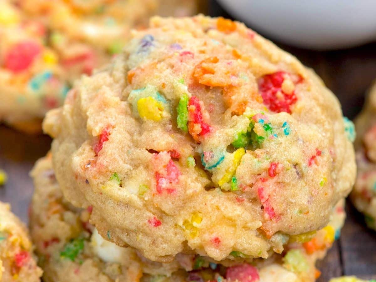 A close-up of a soft, chewy cookie filled with colorful bits of cereal, giving it a vibrant and textured appearance. The cookie looks homemade and has a golden brown color with visible colorful specks throughout.