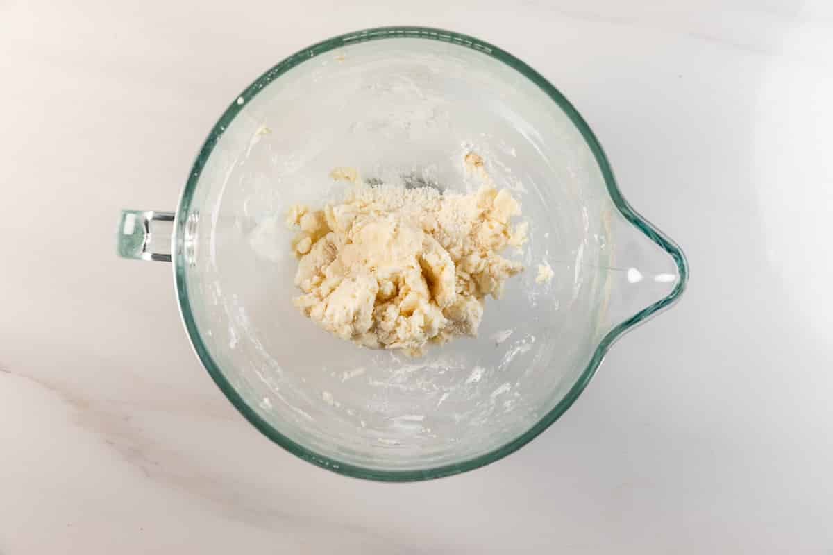 Meilleures barres de biscuits au sucre – Fou de croûte 9 Un bol à mélanger en verre contenant de la pâte ou un mélange partiellement mélangé repose sur une surface blanche. Un peu de farine et de pâte apparaissent sur les bords du bol.