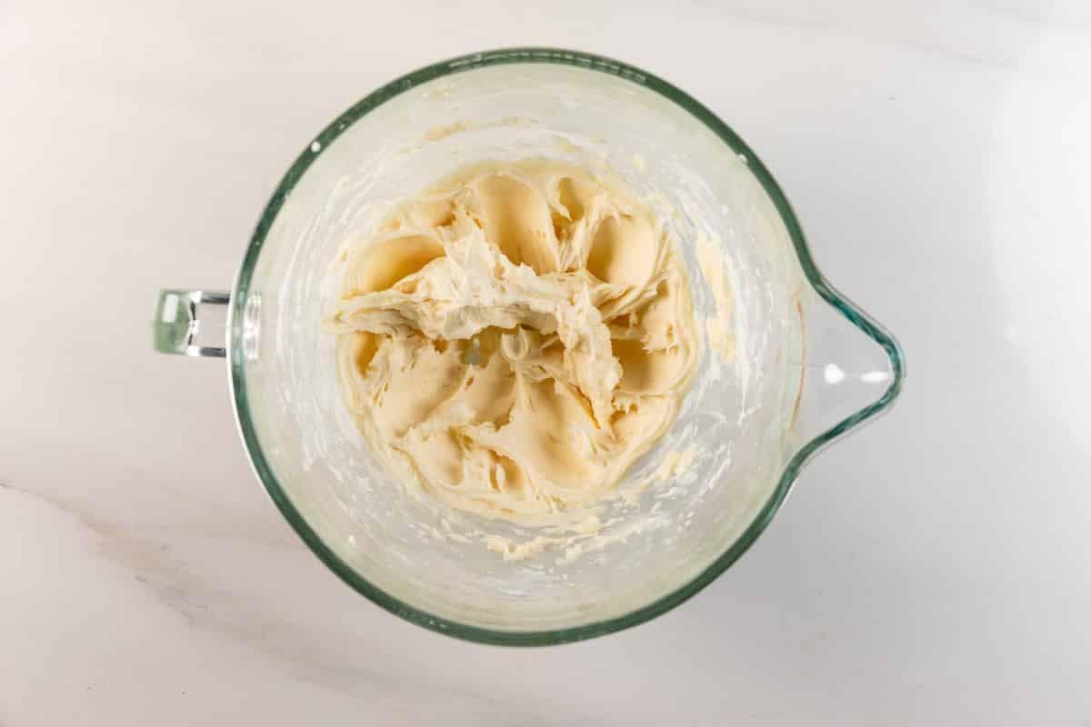 Meilleures barres de biscuits au sucre – Fou de croûte 10 Un bol à mélanger en verre rempli de pâte à biscuits à la crème jaune vif se trouve sur un comptoir blanc.