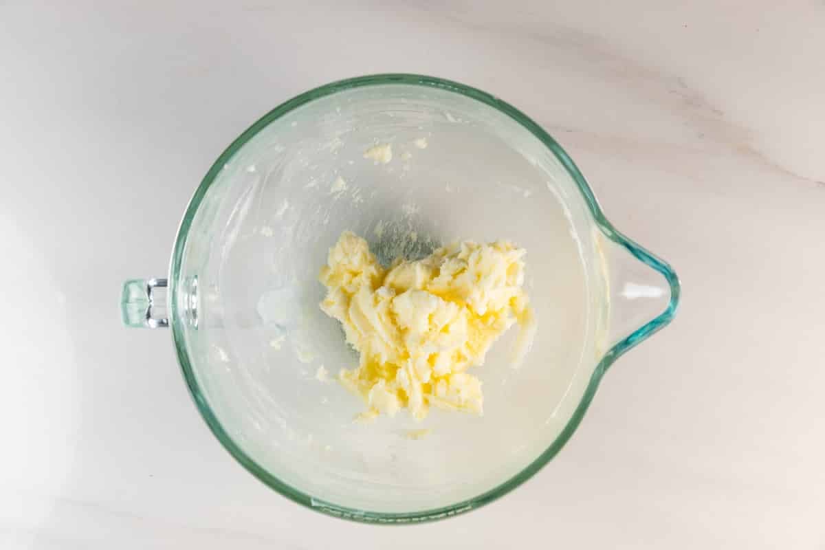 Meilleures barres de biscuits au sucre – Fou de croûte 13 Un bol à mélanger en verre avec une petite quantité de beurre et de sucre au fond, posé sur un plan de travail blanc.