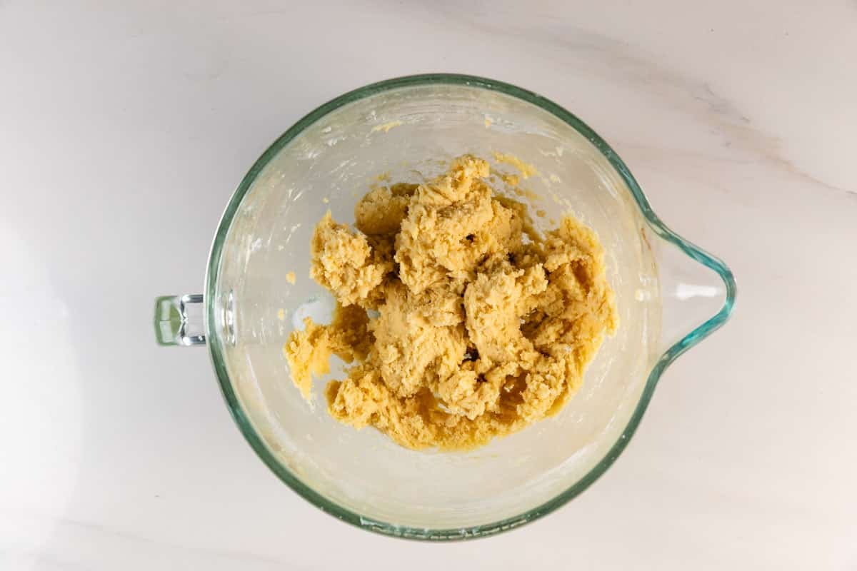 Meilleures barres de biscuits au sucre – Fou de croûte 11 Un bol à mélanger en verre rempli de pâte à biscuits jaune repose sur un comptoir en marbre blanc.