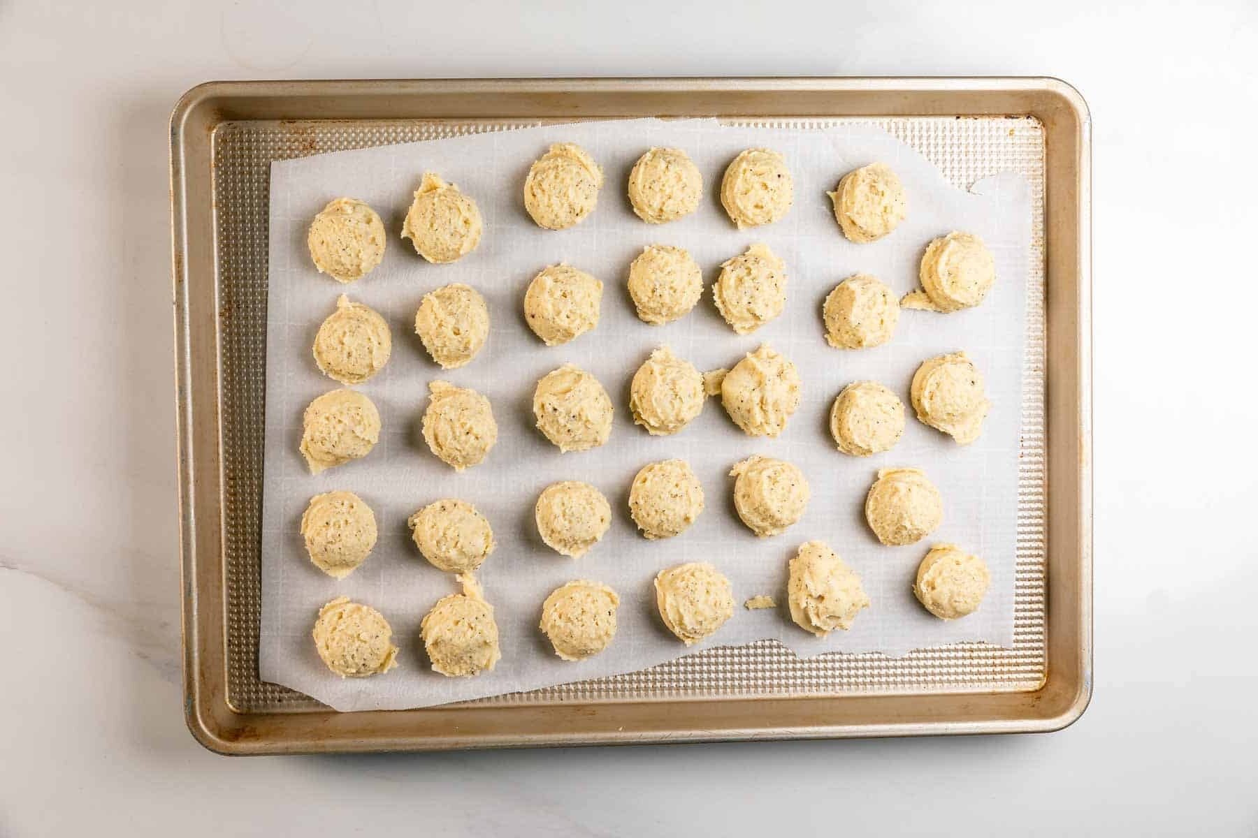 A baking sheet lined with parchment paper holds 28 evenly spaced scoops of unbaked cookie dough, arranged in rows, ready to be baked.
