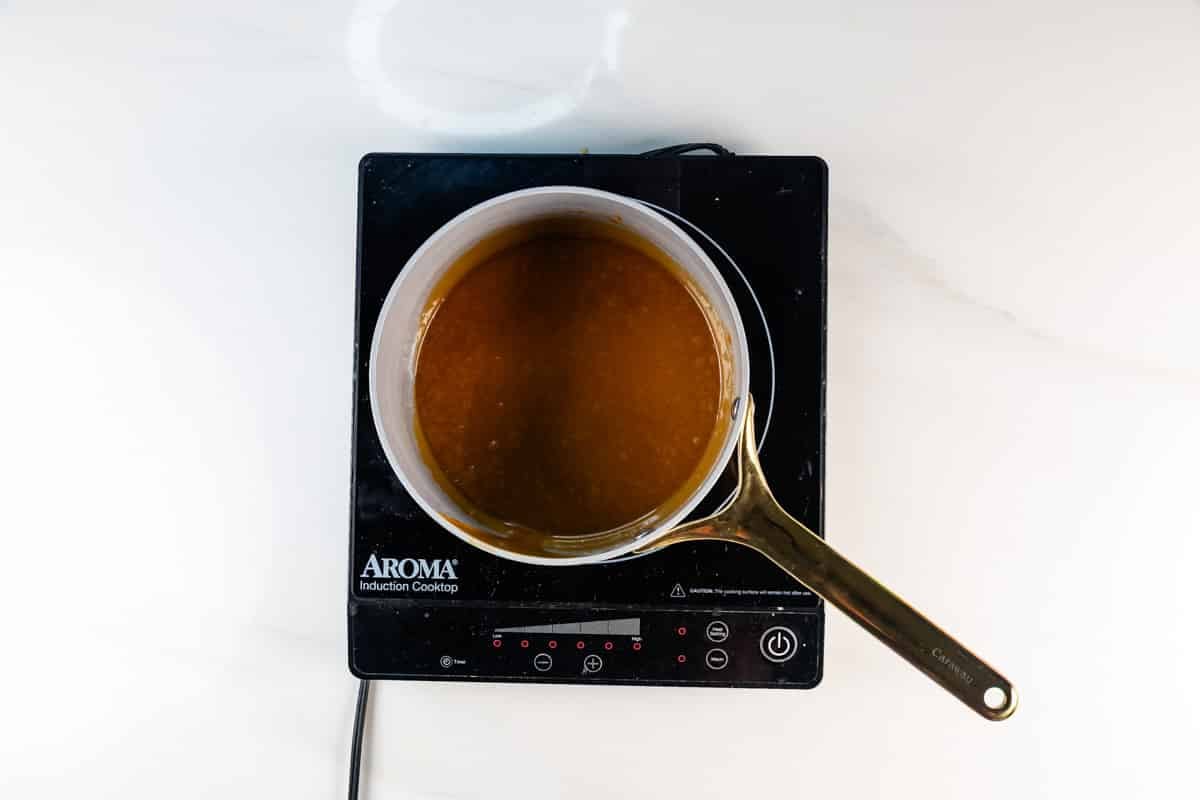 A saucepan with brown sauce sits on an Aroma induction cooktop on a white countertop, viewed from above.