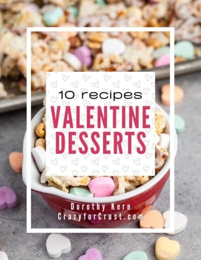 A red bowl filled with Valentine’s-themed snack mix, including heart-shaped candies and marshmallows, sits on a gray surface. In the background is a tray of more snack mix. Text overlay: 10 recipes Valentine Desserts.