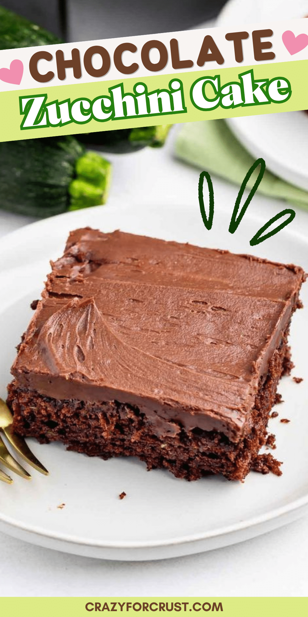 A slice of chocolate zucchini cake with thick chocolate frosting sits on a white plate with a fork. The image is labeled Chocolate Zucchini Cake and shows part of a zucchini in the background.
