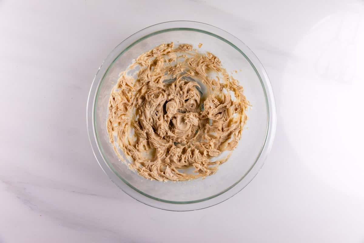 A glass bowl filled with creamed butter and sugar mixture sits on a white marble surface, ready for baking.