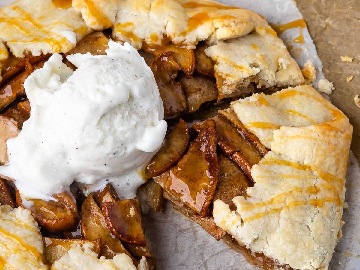 Galette rustique aux pommes à la croûte dorée, fourrée de tranches de pommes épicées à la cannelle, surmontée d'une boule de glace vanille et arrosée de sauce caramel. Une tranche a été coupée et légèrement arrachée.