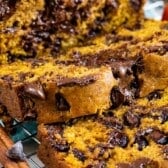 Close-up of sliced pumpkin bread with melted chocolate chips on a cooling rack, with cinnamon sticks and a small decorative pumpkin in the background.