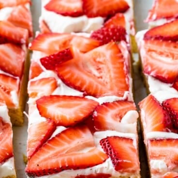 Rectangular dessert bars topped with a layer of white frosting and fresh sliced strawberries, arranged closely together on a tray.