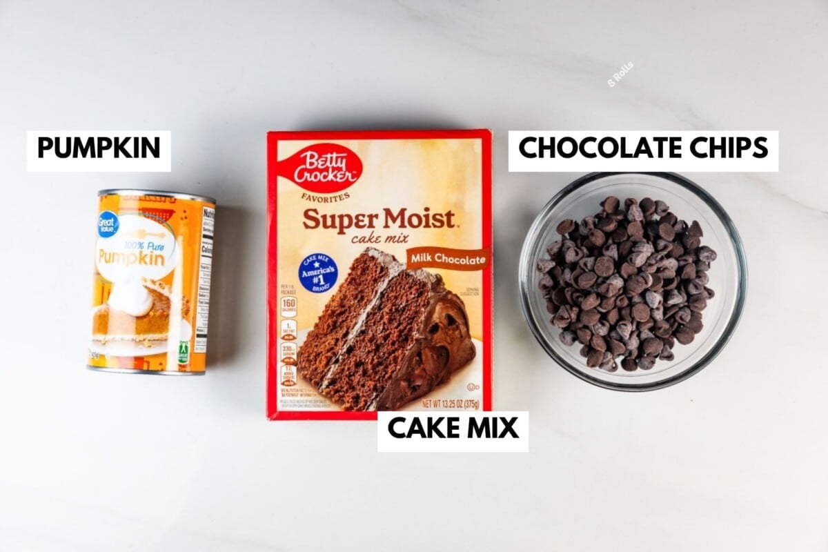 A can of pumpkin, a box of milk chocolate cake mix, and a bowl of chocolate chips are arranged on a white surface with labels identifying each item.