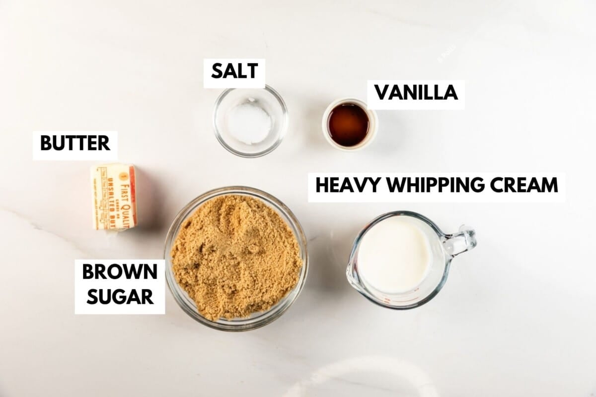 Top-down view of labeled ingredients on a white surface: butter, brown sugar, salt, vanilla, and heavy whipping cream in separate containers.