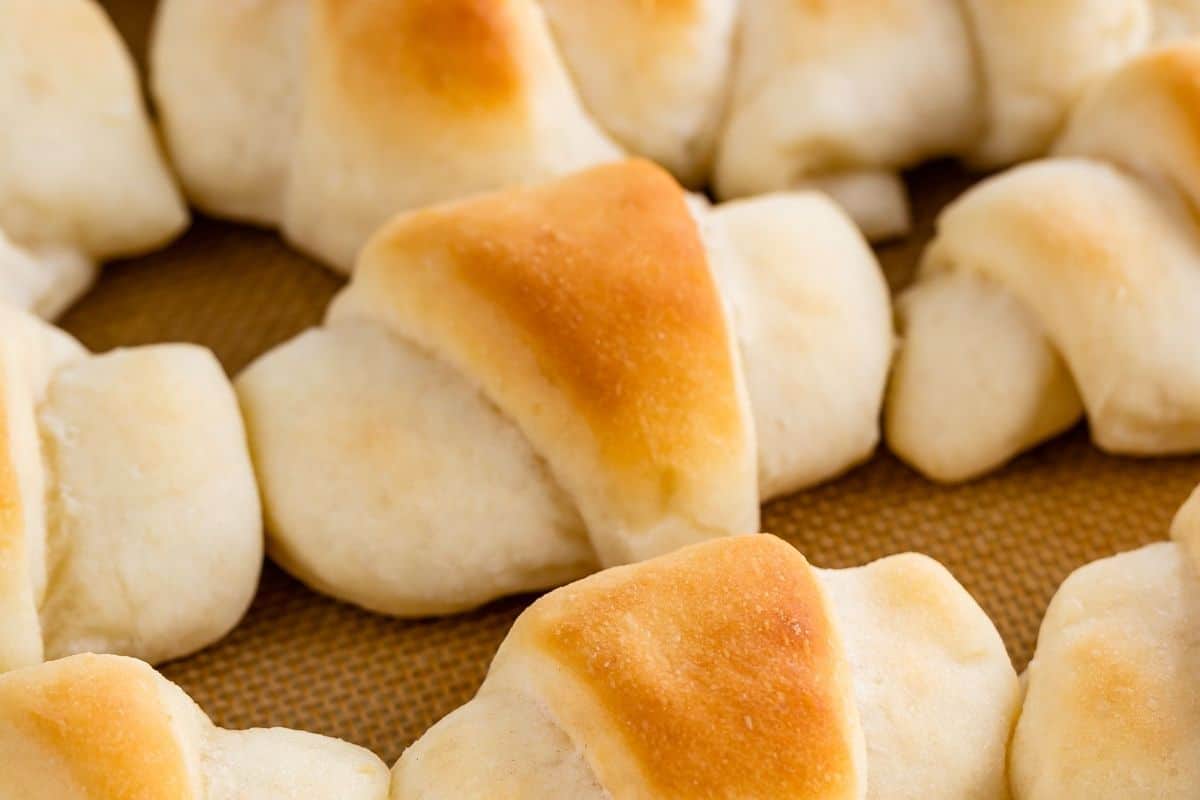 Golden brown, homemade crescent rolls arranged in a circle on a baking sheet, showing their fluffy, soft texture and slightly crisp tops.