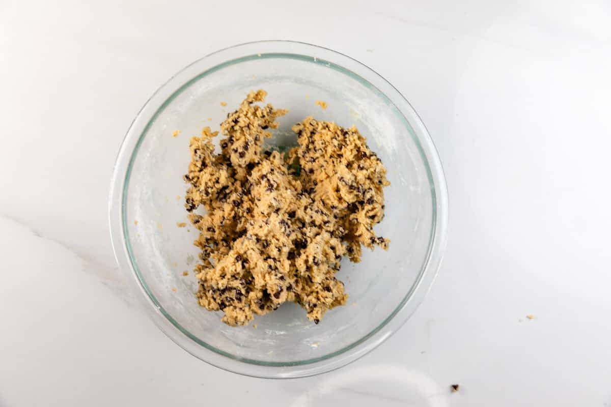 A glass bowl filled with chocolate chip cookie dough sits on a white countertop.