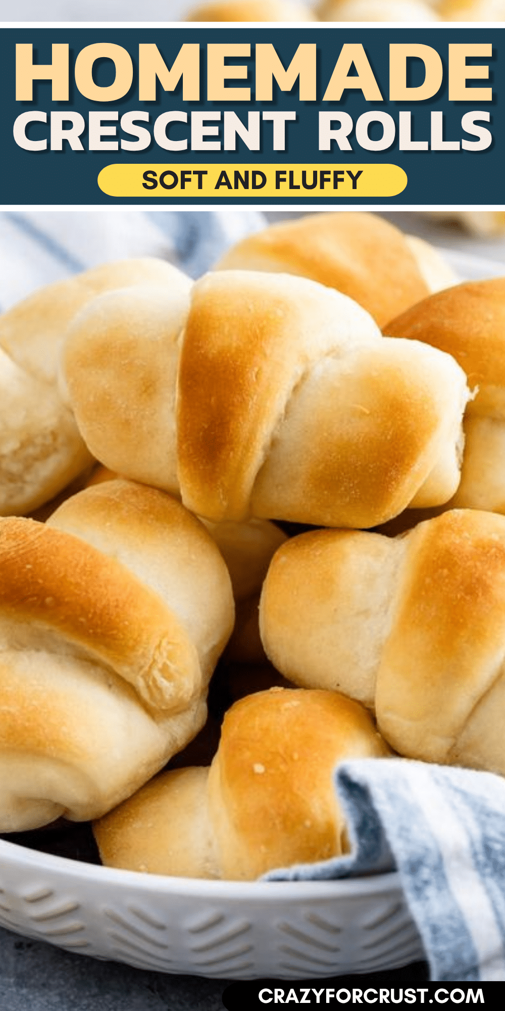 A pile of homemade crescent rolls on a plate, golden brown and fluffy, with a blue and white striped towel partially visible in the corner.