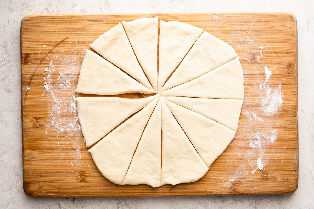 Round dough cut into twelve triangle-shaped pieces on a floured wooden cutting board.