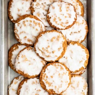 A baking sheet filled with round oatmeal cookies, each covered with a shiny layer of white icing. The cookies are slightly overlapping and arranged in a neat pile.