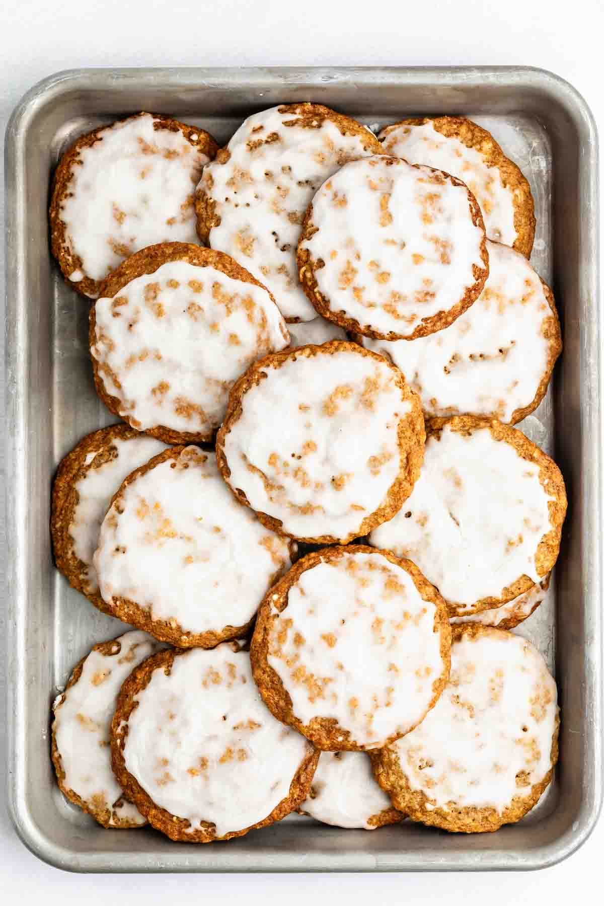 A baking sheet filled with round oatmeal cookies, each covered with a shiny layer of white icing. The cookies are slightly overlapping and arranged in a neat pile.