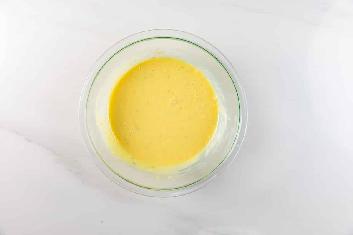 A glass bowl filled with smooth, yellow cake batter sits on a white countertop.