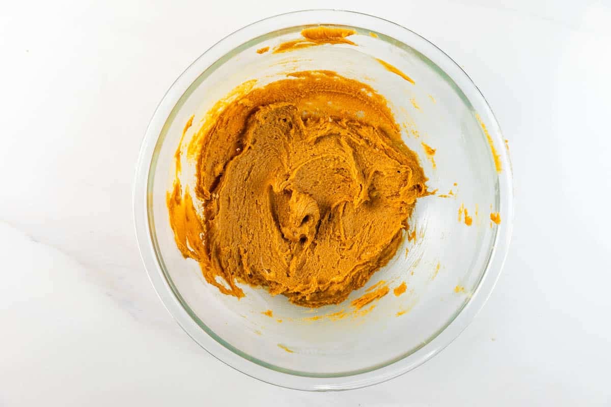 A glass bowl filled with a smooth, orange-brown dough or batter mixture, placed on a white surface.