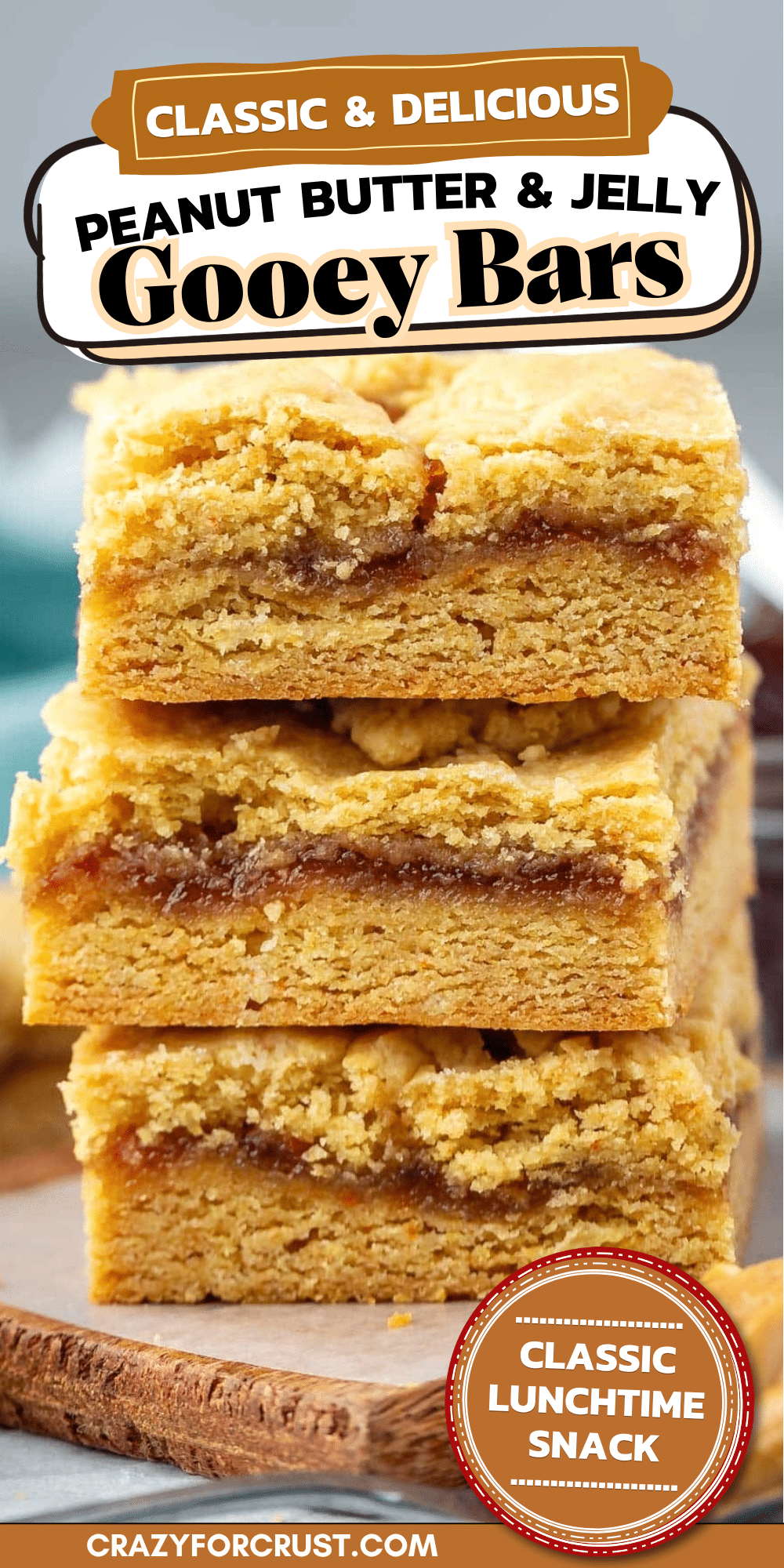 Three thick, crumbly peanut butter and jelly bars are stacked on a wooden board. The bars have visible layers of peanut butter cookie and red jelly filling.