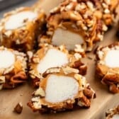 Sliced pieces of caramel-wrapped marshmallows coated in chopped pecans are arranged on a wooden board, showcasing their creamy, nutty texture and sweet, chewy appearance.