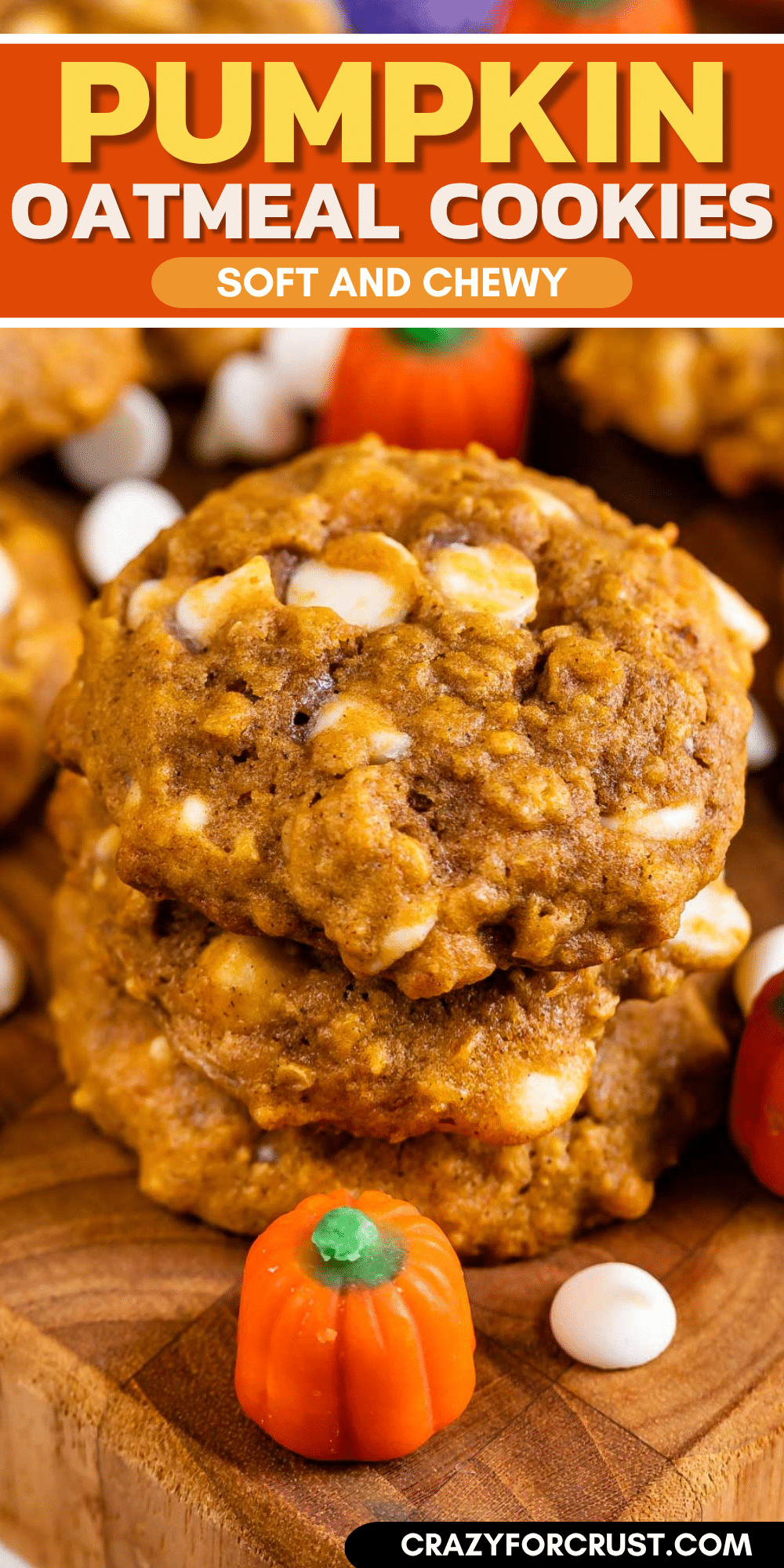 Stack of pumpkin oatmeal cookies with white chocolate chips on a wooden board, surrounded by small candy pumpkins and white candies. Text overlay reads: Pumpkin Oatmeal Cookies, Soft and Chewy.