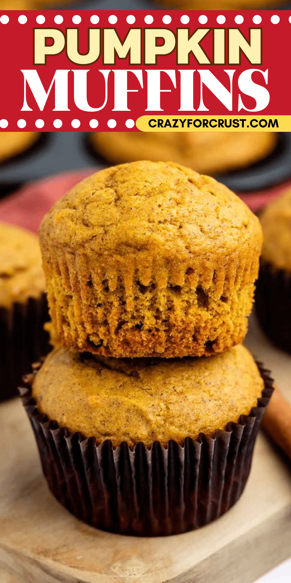 Two pumpkin muffins, one stacked on top of the other, sit on a wooden board. The background shows more muffins and a cinnamon stick. The image header reads Pumpkin Muffins with the website crazyforcrust.com.