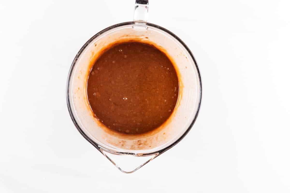 A glass mixing bowl filled with chocolate batter sits on a white surface, viewed from above.