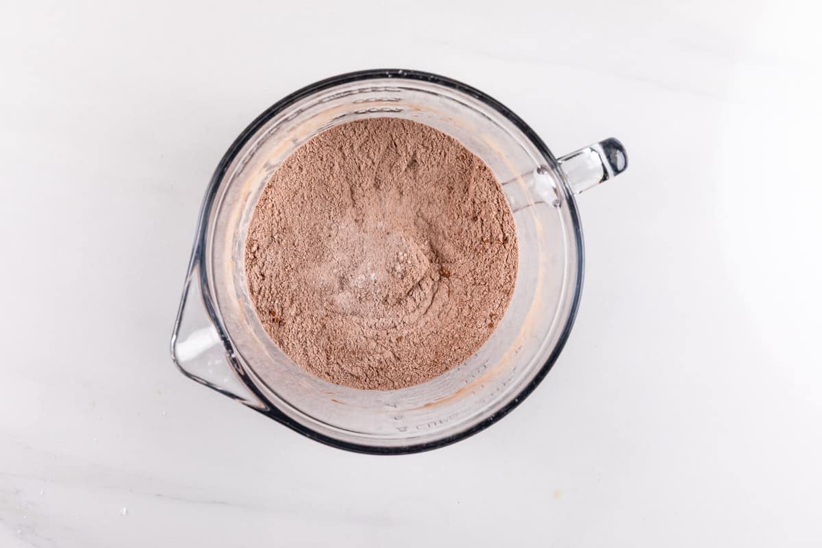 A glass mixing bowl filled with light brown cocoa powder mixture sits on a white countertop, viewed from above.