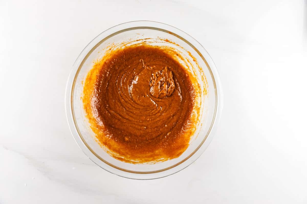 A glass bowl filled with smooth, brown pumpkin bread batter sits on a white countertop.